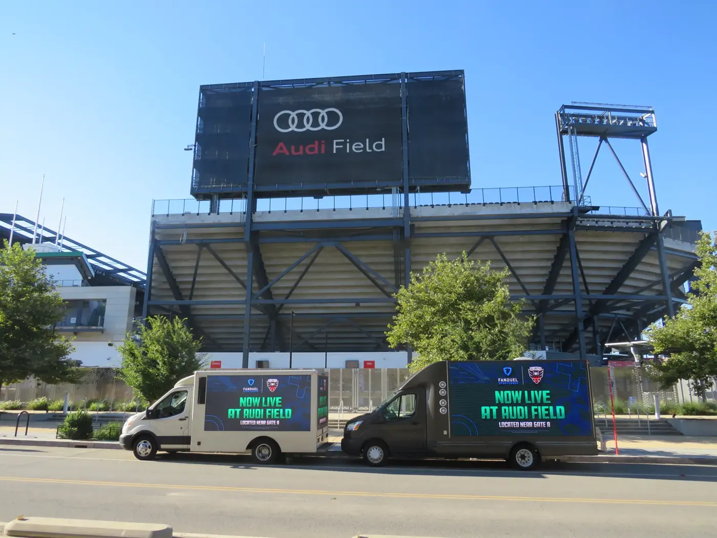 Two digital billboard trucks showing “Now Live at Audi Field” parked outside Audi Field in Washington, D.C.