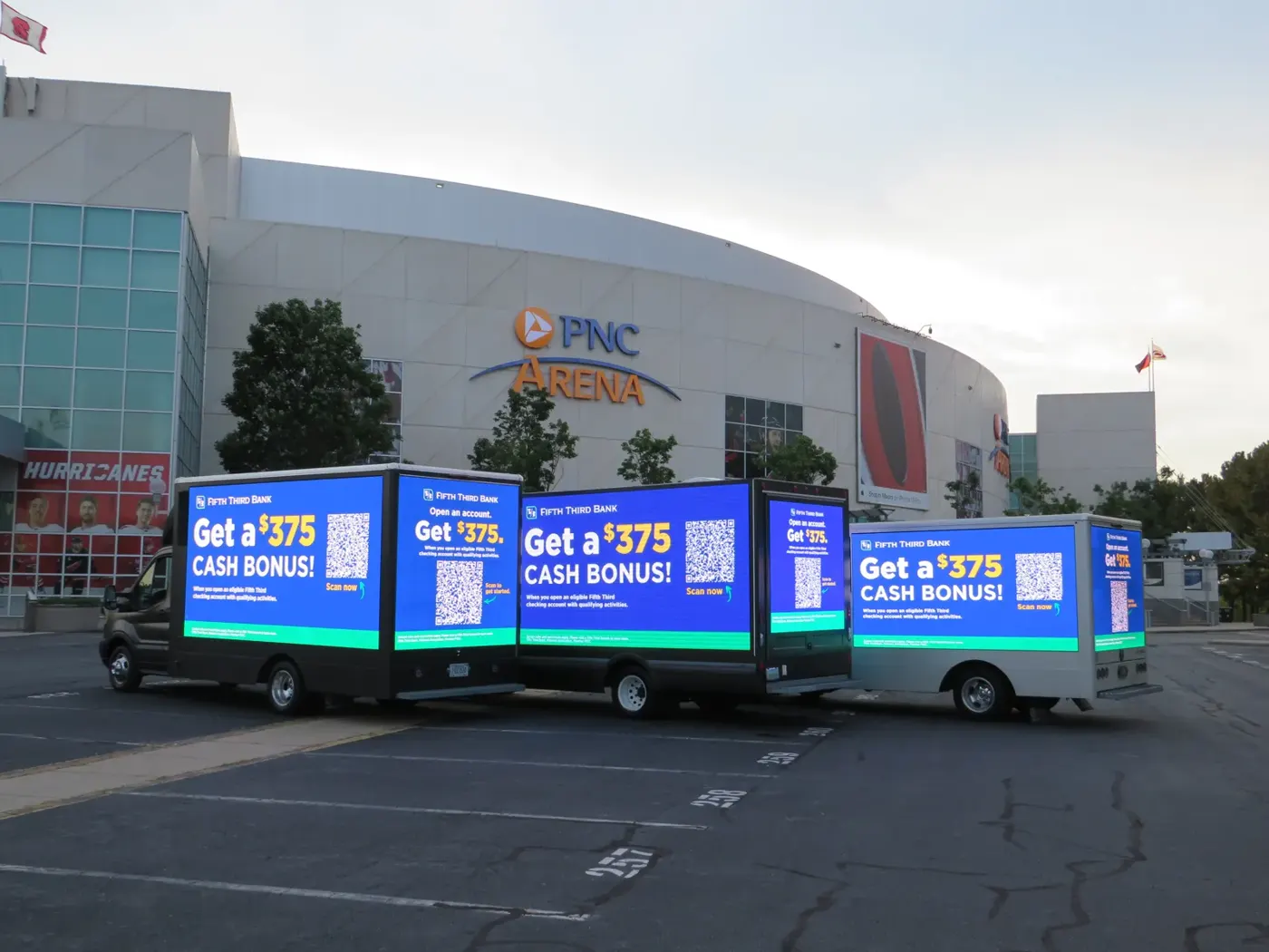 Four Fifth Third Bank digital billboard trucks lined up outside an arena showing “Get a $375 Cash Bonus” with QR codes
