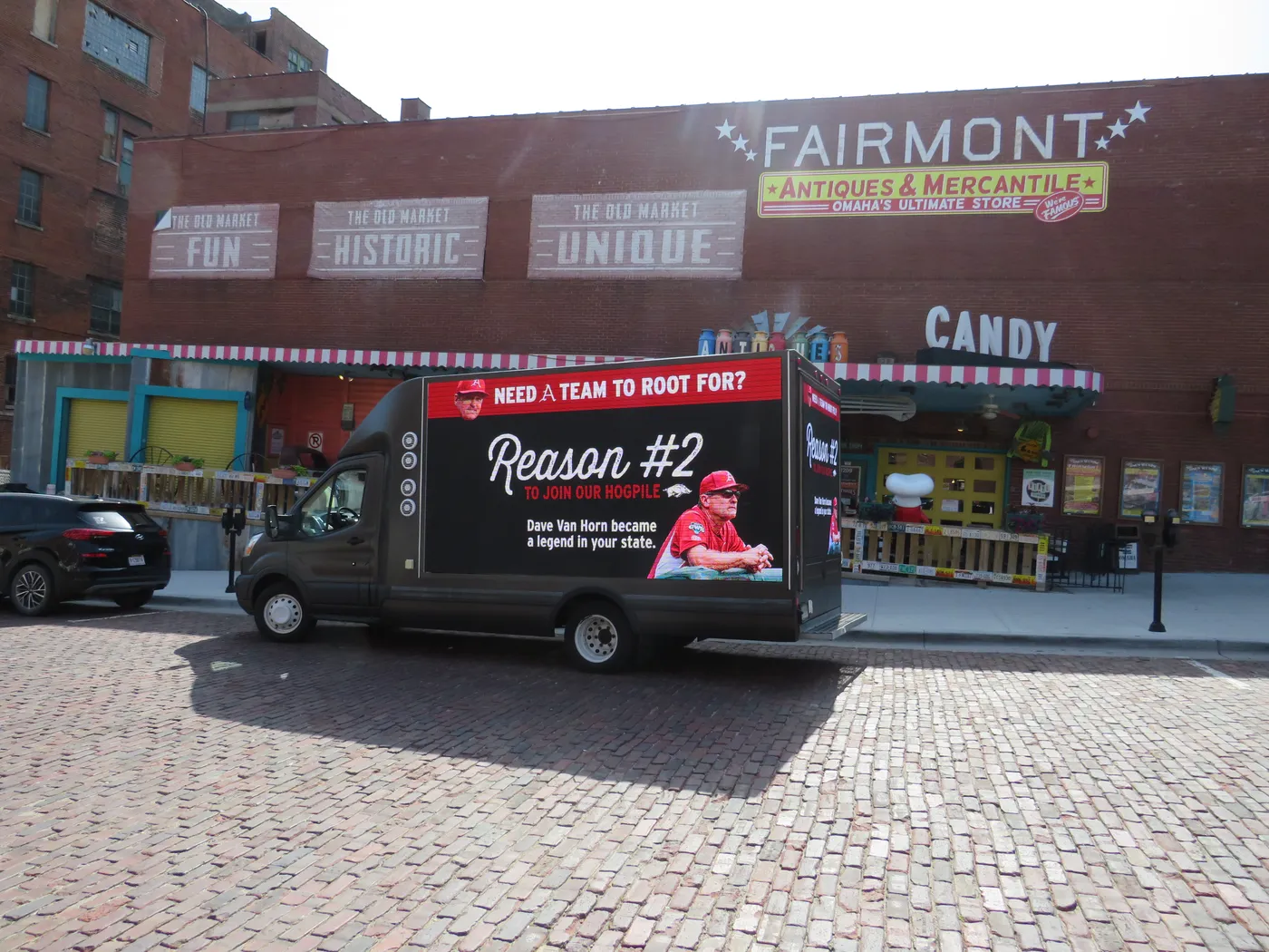 A Razorbacks digital billboard truck showing “Need a Team to Root For? Reason #2” on the brick streets of Omaha’s Old Market