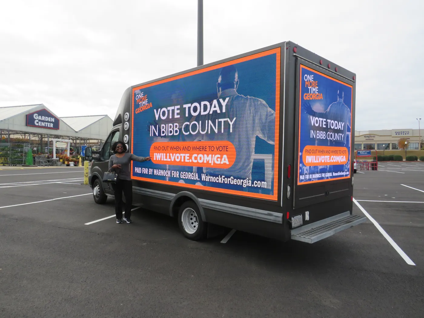 A Warnock for Georgia digital billboard truck showing “Vote Today in Bibb County” in a shopping center parking lot